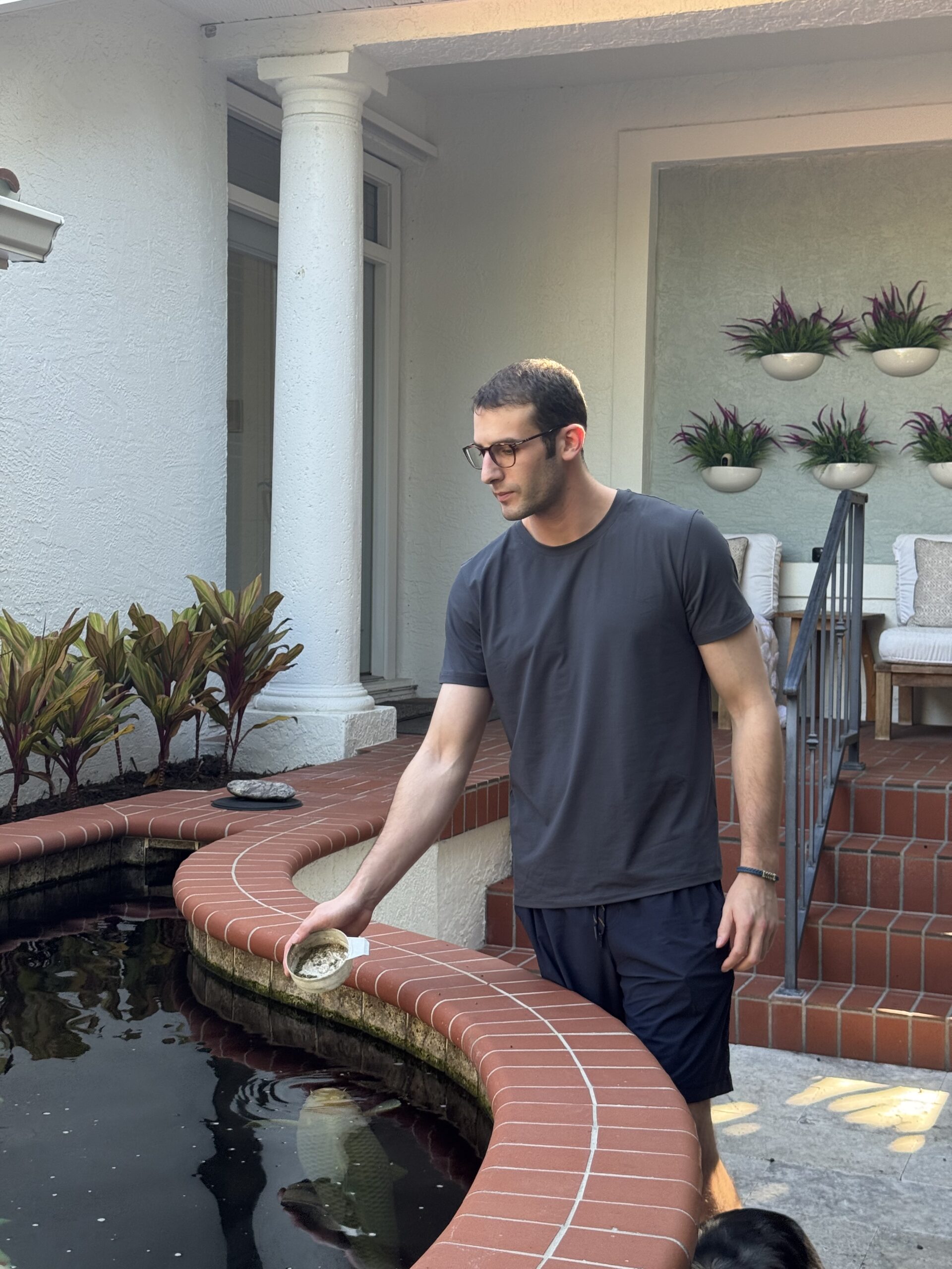 Benjamin Hayt holding a feeding container beside a koi pond