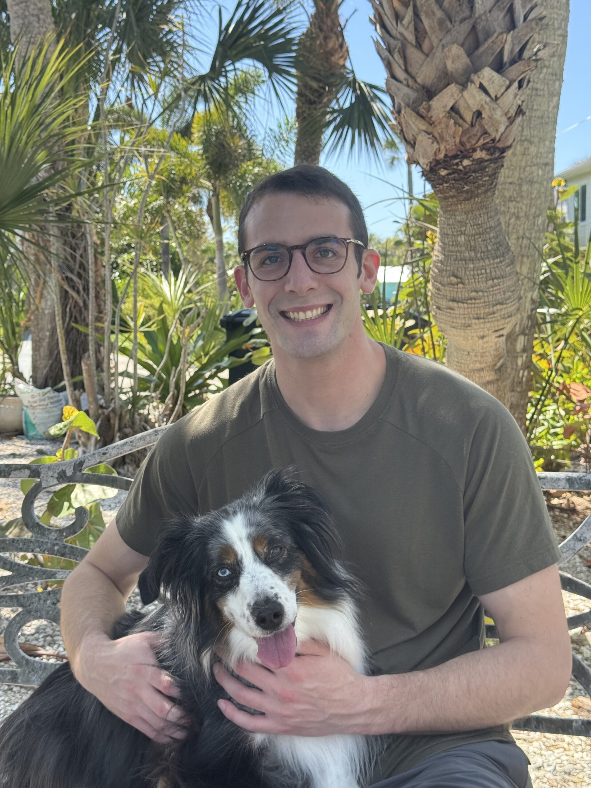 Benjamin Hayt seated outdoors with a black, white and tan dog